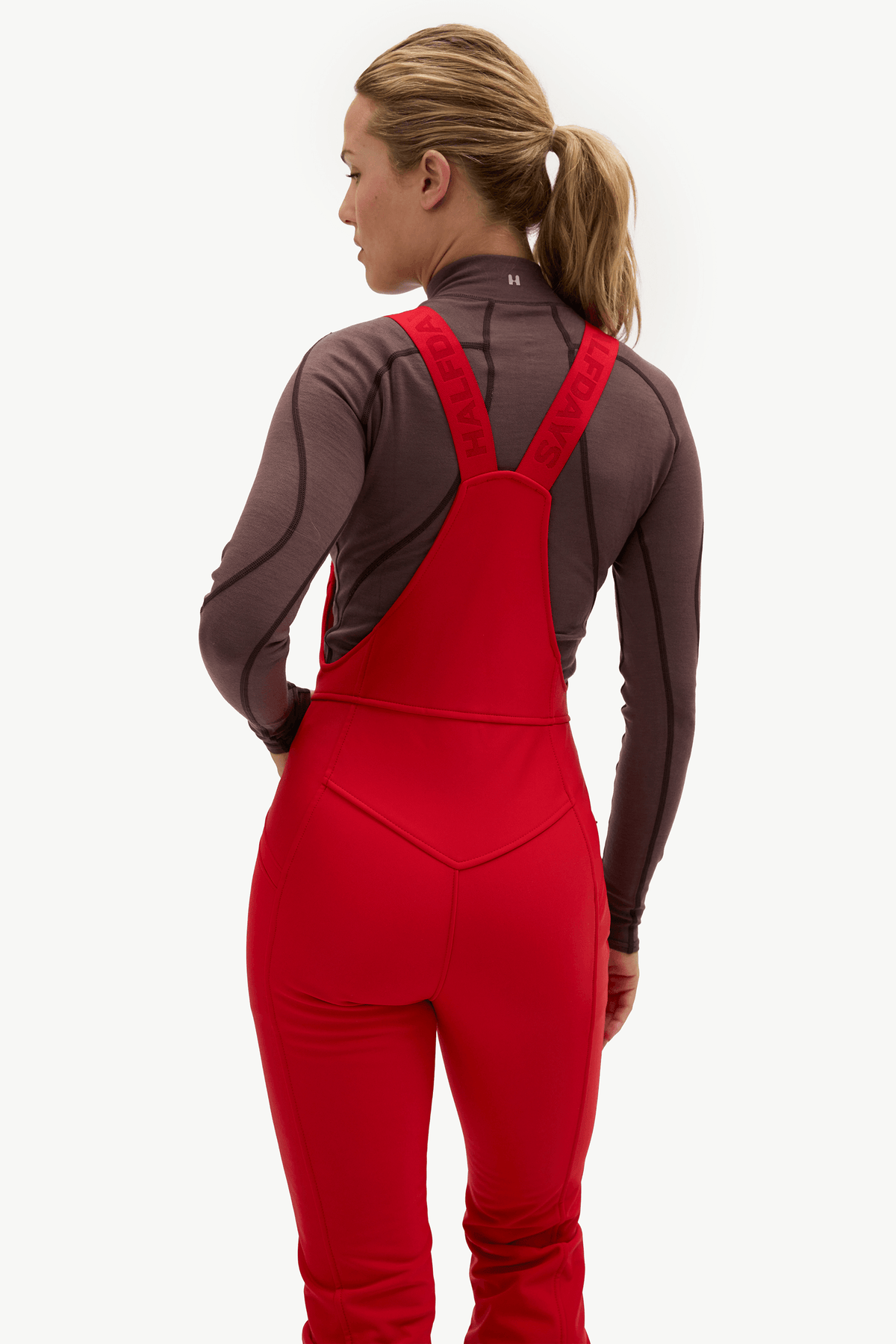 A woman shown from the back wearing a red full-body wetsuit over a dark brown long-sleeve athletic top, photographed against a clean white studio background.