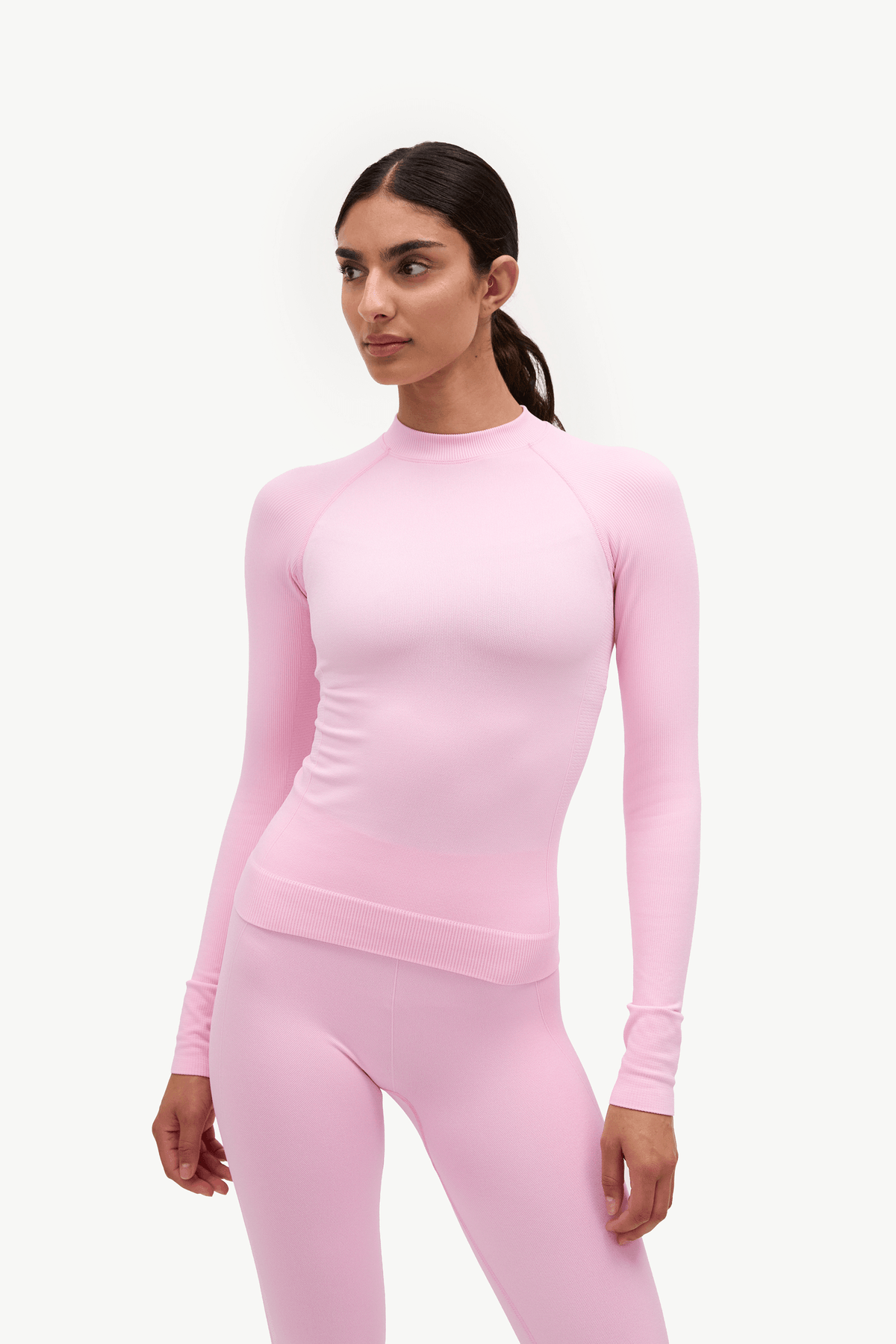 A woman modeling a light pink long-sleeve athletic top and matching pink leggings against a plain white studio background.