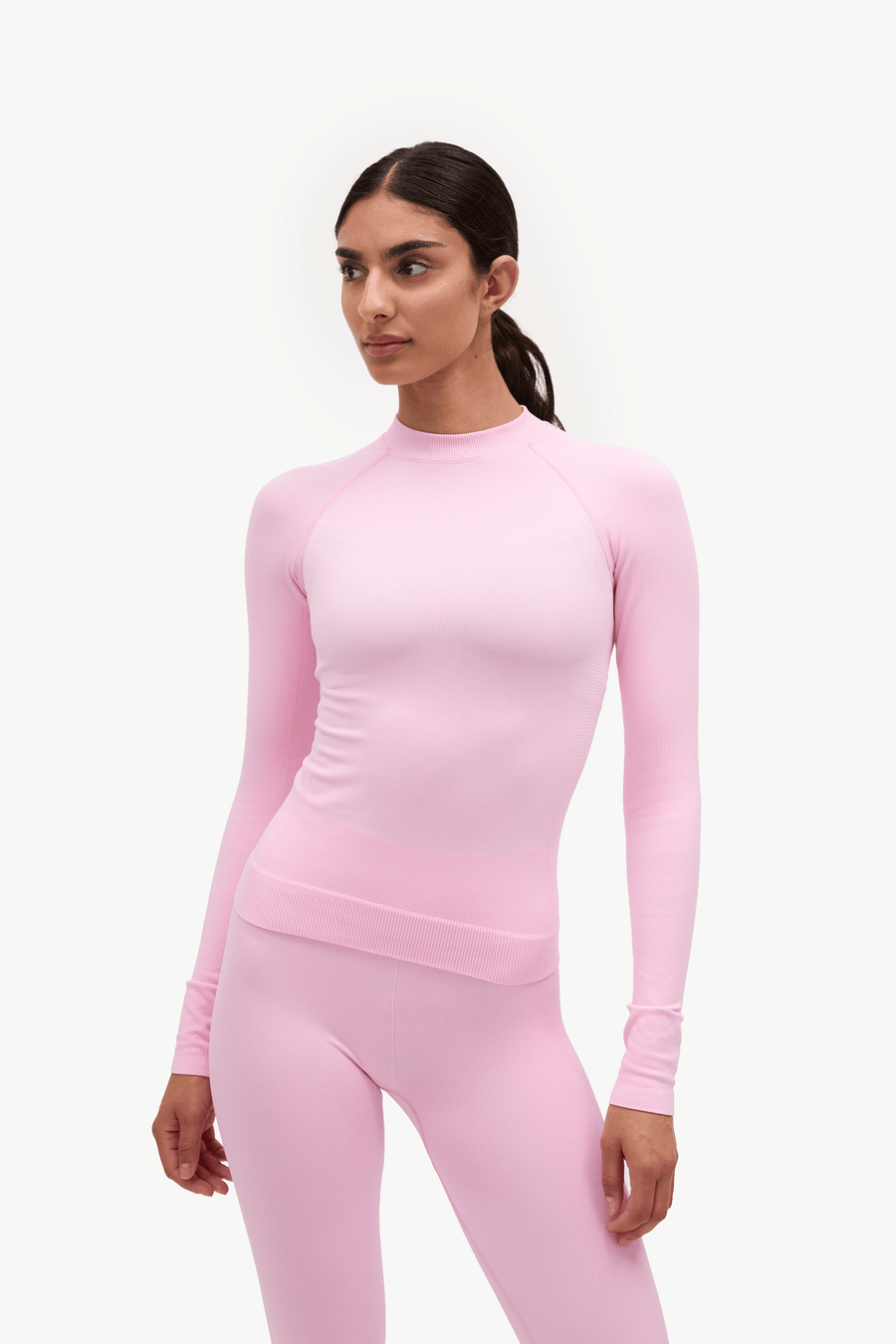 A woman modeling a light pink long-sleeve athletic top and matching pink leggings against a plain white studio background.