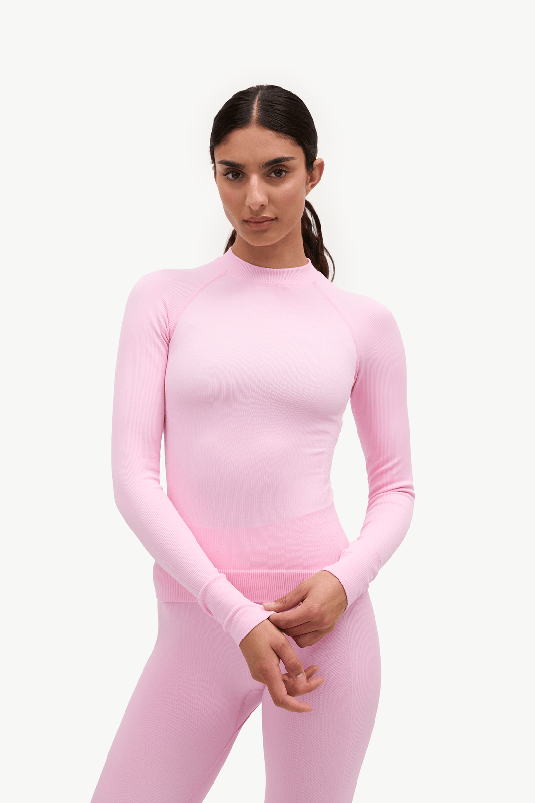 A woman modeling a light pink long-sleeve athletic top and matching pink leggings against a plain white studio background.