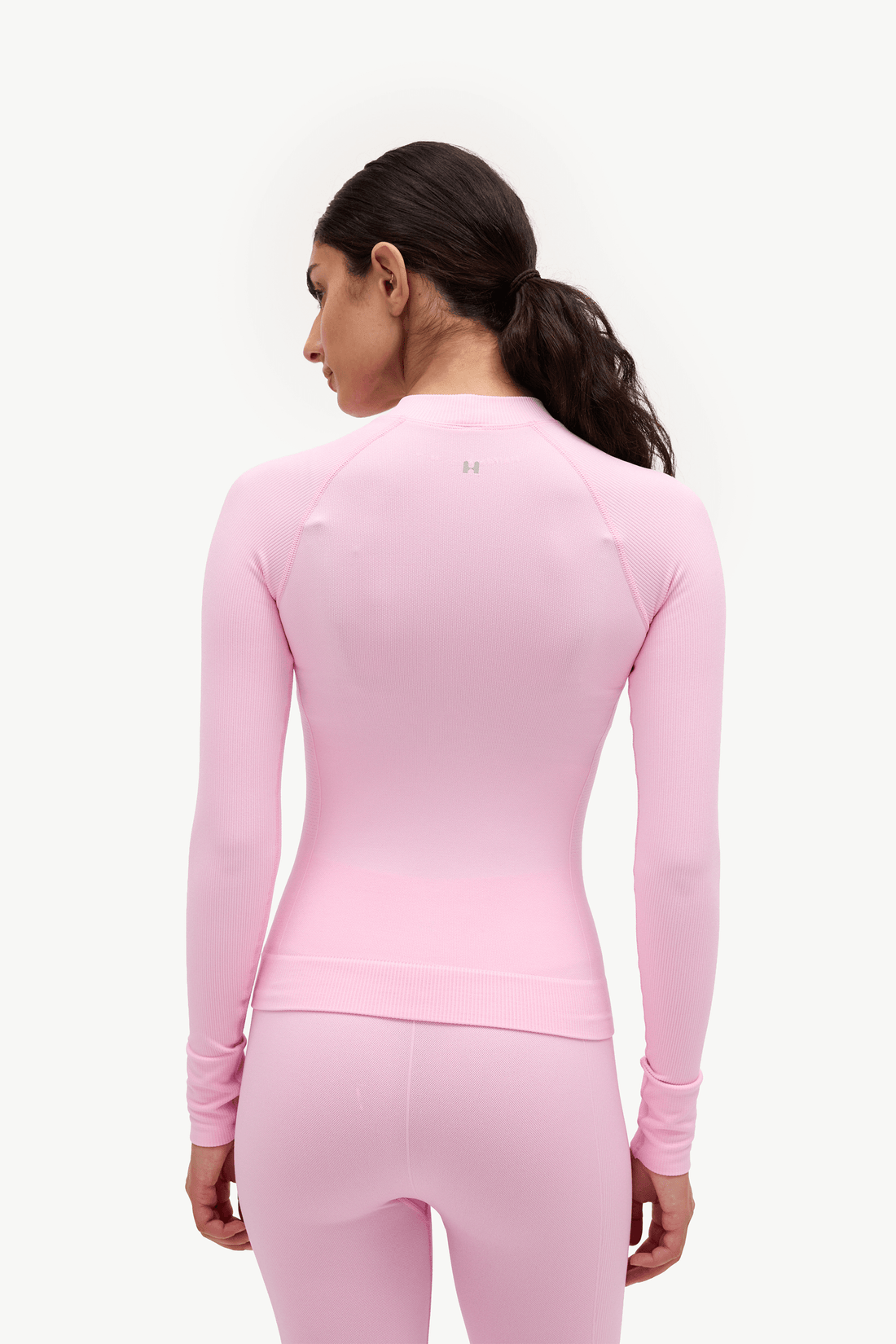 A woman shown from the back wearing a fitted long-sleeve athletic top and matching leggings in light pink, against a plain light background.