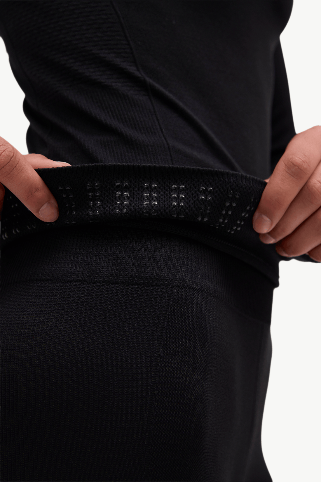 Close-up of a person wearing black athletic leggings and pulling up a matching black waistband with small reflective dots.