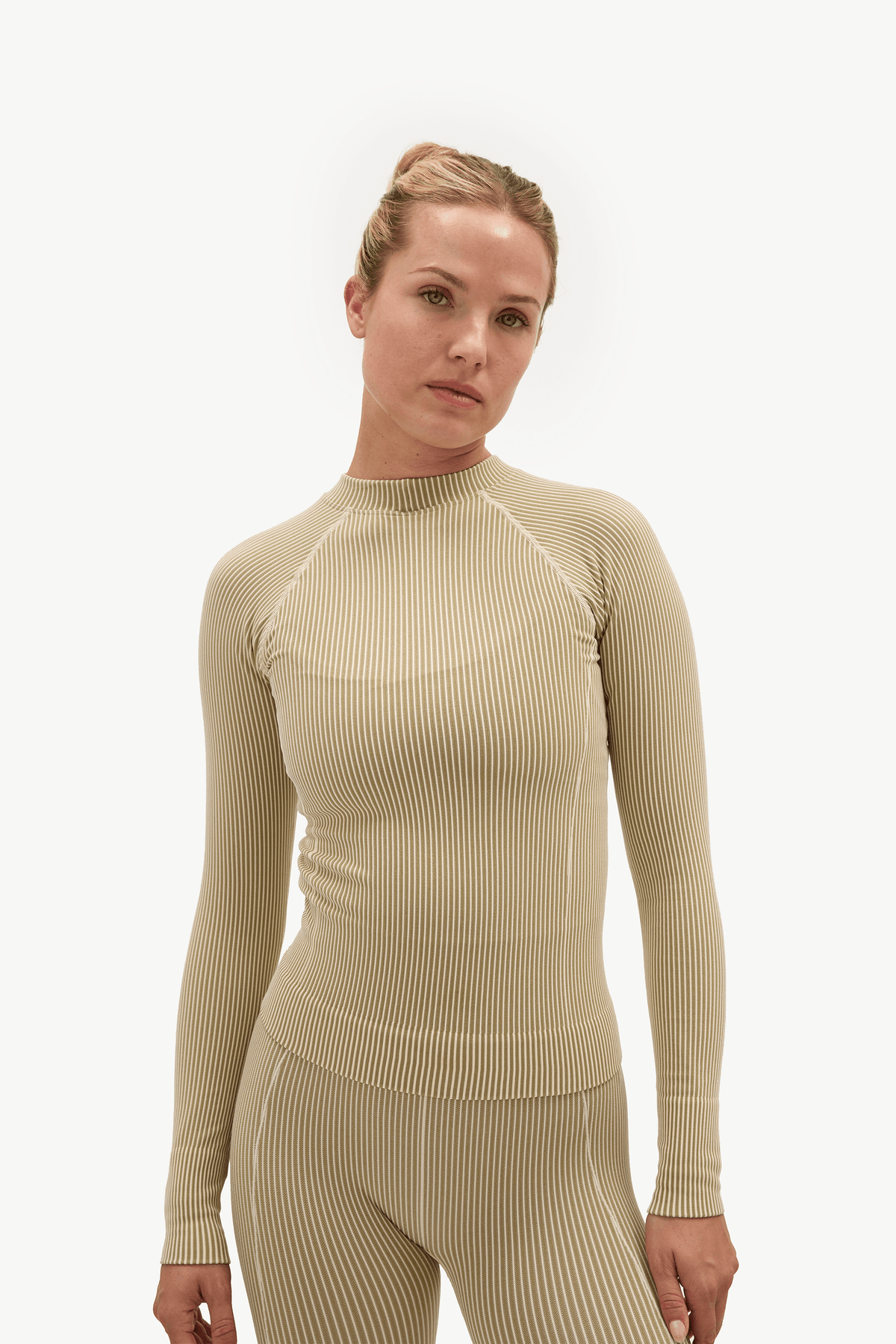 A woman modeling a beige ribbed long-sleeve mock neck top and matching ribbed leggings against a plain white studio background.