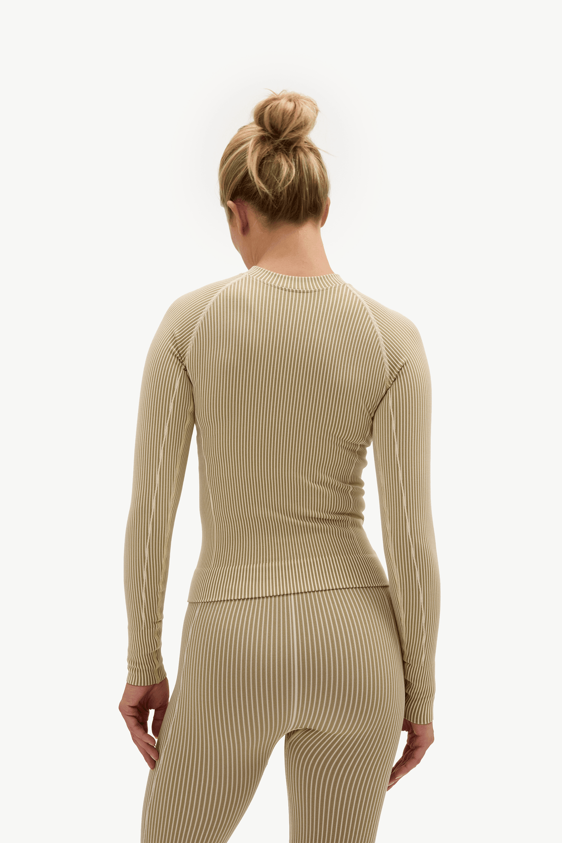 A woman viewed from the back wearing a ribbed long-sleeve top and matching leggings in a light beige/khaki color, set against a plain white studio background.