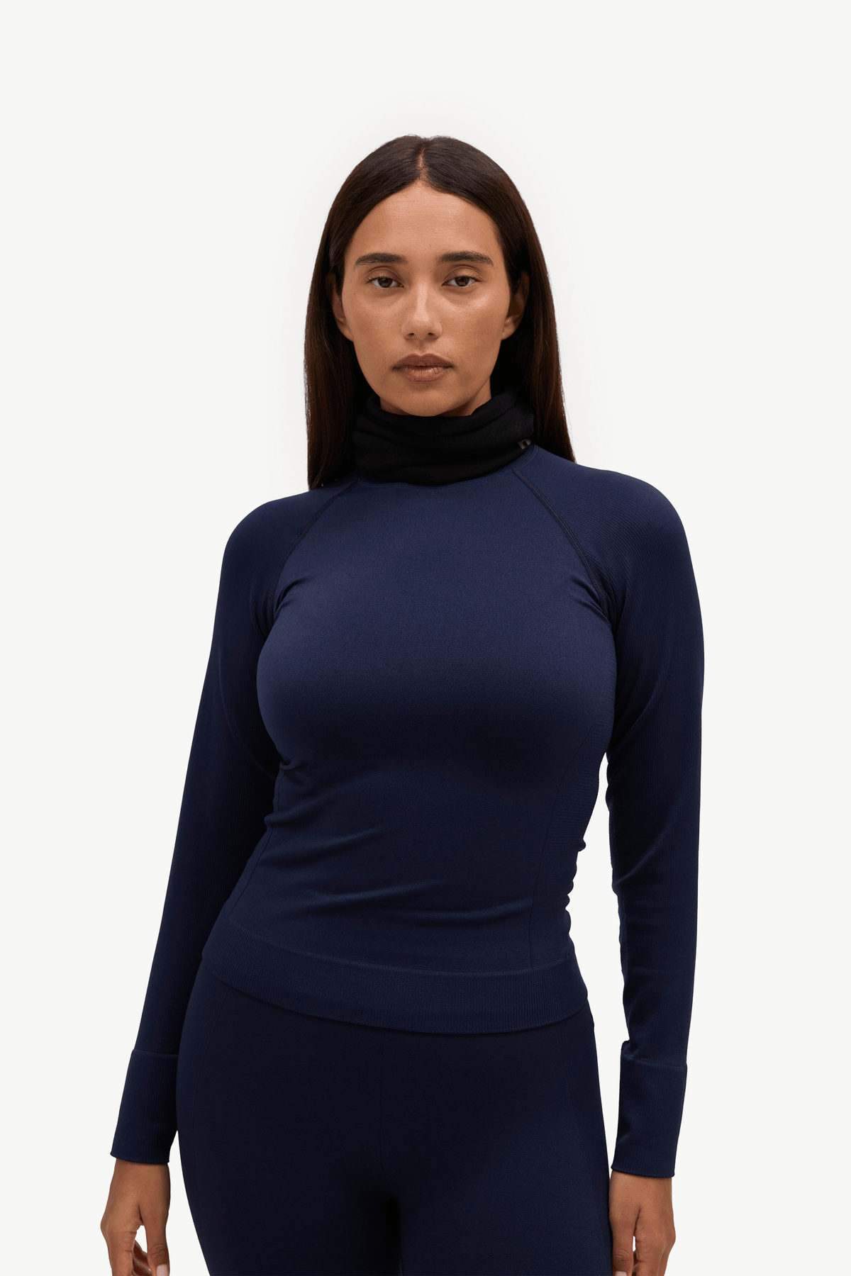 A woman modeling a dark navy blue long-sleeve athletic top with a high mock neck, paired with matching leggings, against a plain white studio background.