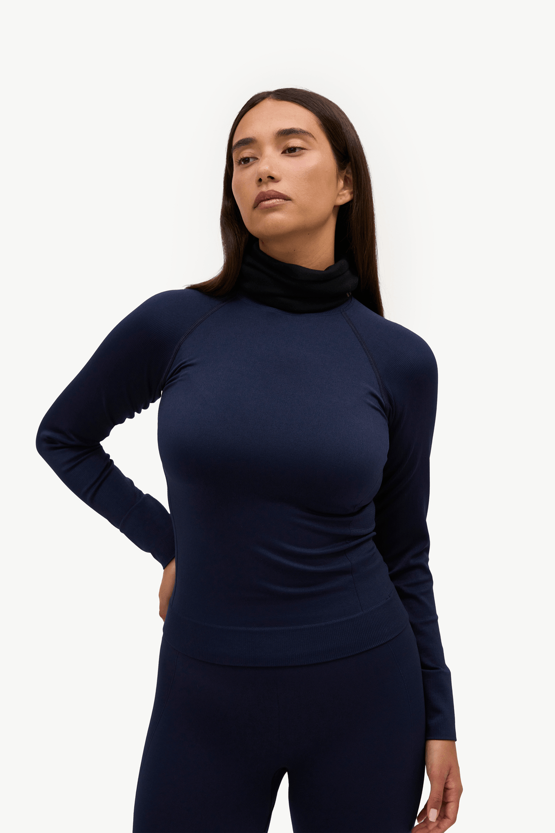 A woman modeling a dark navy blue long-sleeve turtleneck athletic top and matching leggings against a clean white studio background.