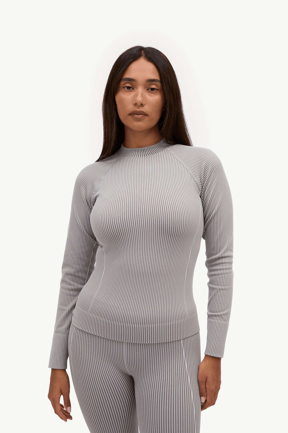 A woman modeling a light gray ribbed knit long-sleeve top and matching ribbed leggings against a plain white studio background.