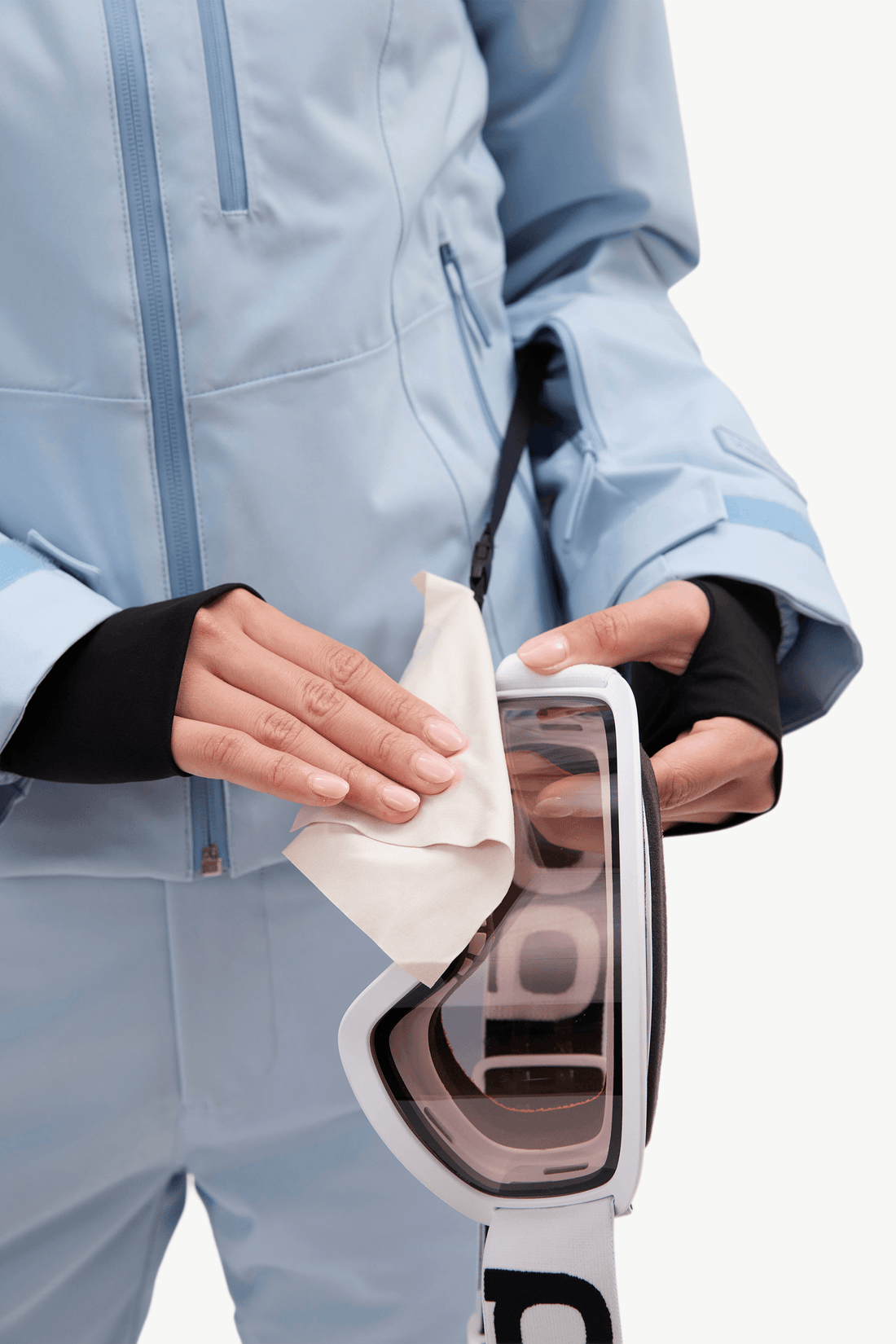 A model wearing a light blue ski jacket and matching pants, holding goggles against a plain white studio background.
