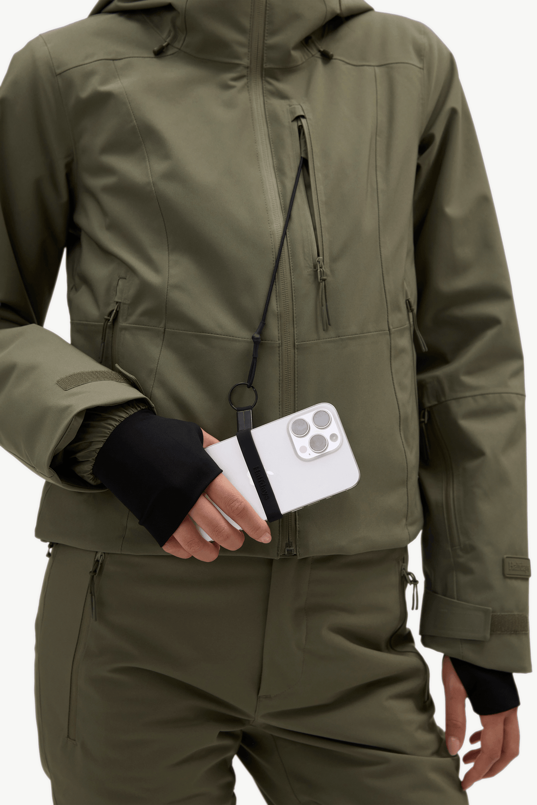 A model stands against a plain white studio background wearing an olive green ski jacket and matching ski pants.