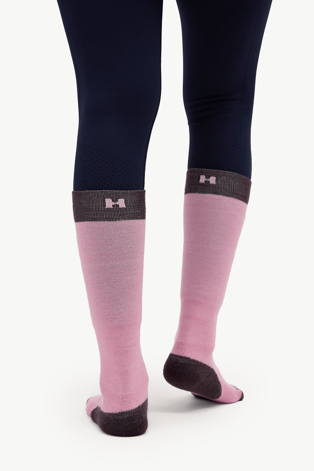 Pink knee-high compression socks with dark gray cuffs and heels, worn with navy blue leggings against a light gray background.