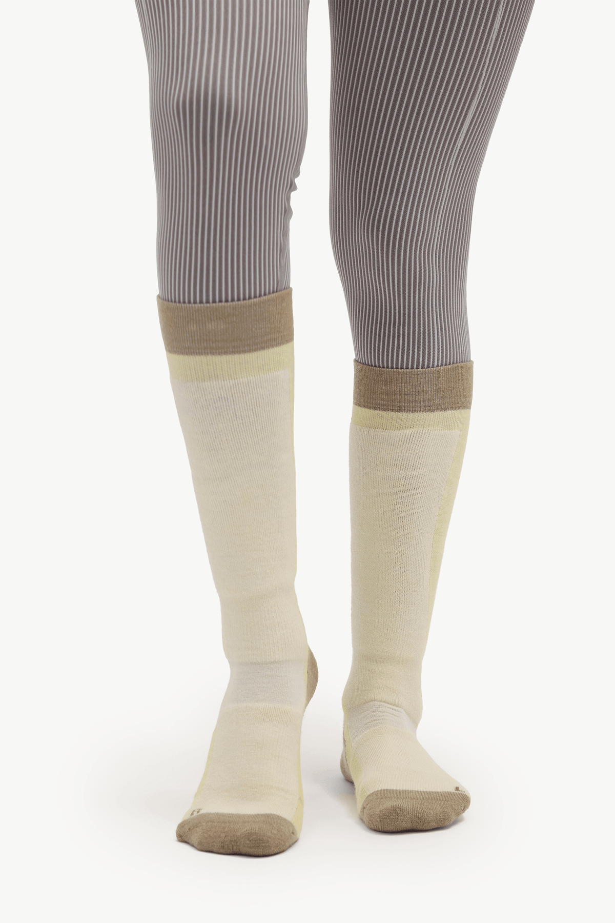 A pair of knee-high compression socks in beige and pale yellow, worn with gray ribbed tights against a white studio background.