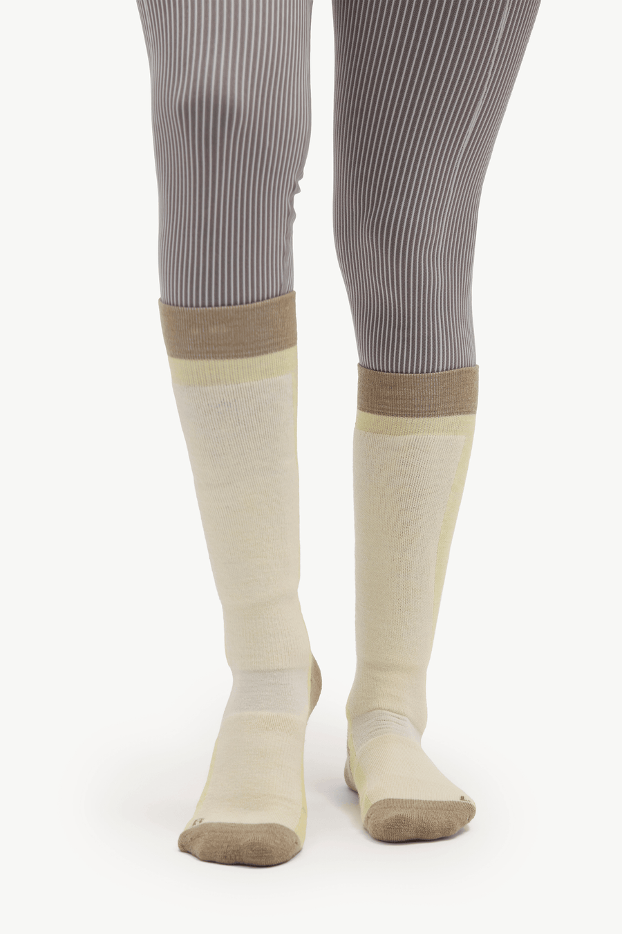 A pair of knee-high compression socks in beige and pale yellow, worn with gray ribbed tights against a white studio background.