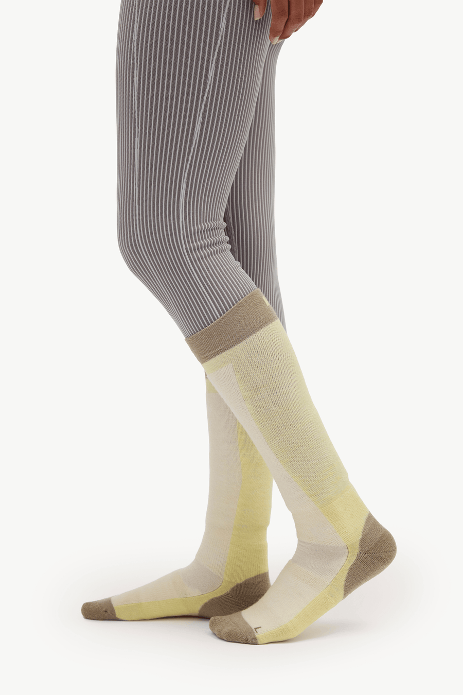 A person wearing ribbed gray tights and knee-high compression socks in pale yellow, cream, and taupe, shown from the knees down against a plain light background.