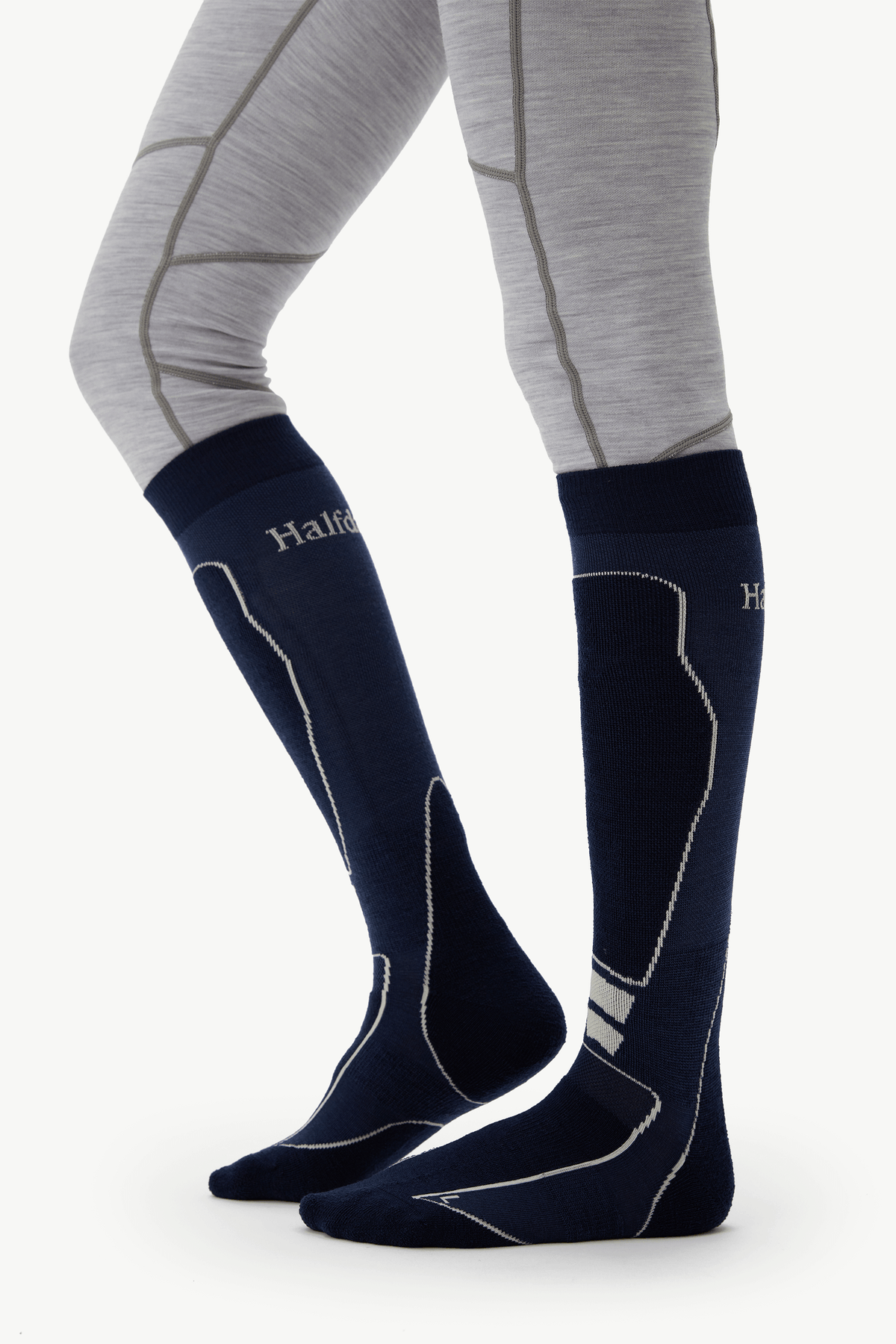 A close-up of a person's lower legs wearing dark navy knee-high athletic socks with white contrast stitching and the brand name 'Halfpipe' visible on the side, paired with light gray compression leggings.