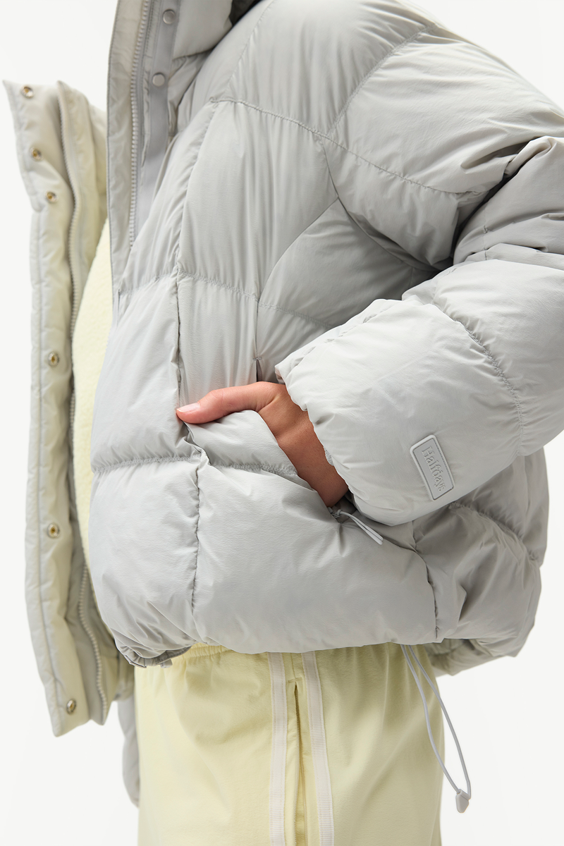 Close-up of the light gray Louise Down Jacket showing the quilted construction, sleeve detail, and hand pocket.