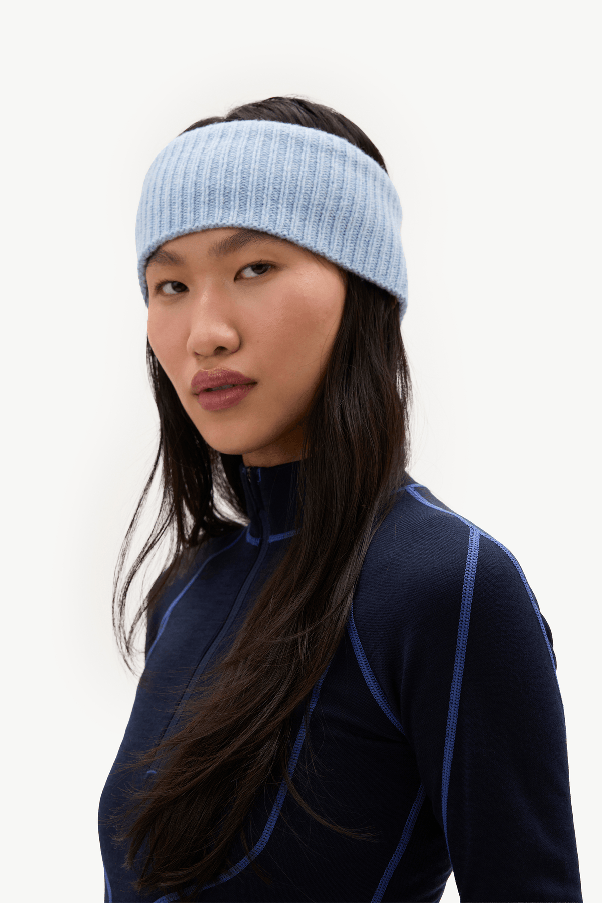 A woman wearing a light blue ribbed knit headband and a dark navy athletic top with blue piping, photographed against a clean white studio background.