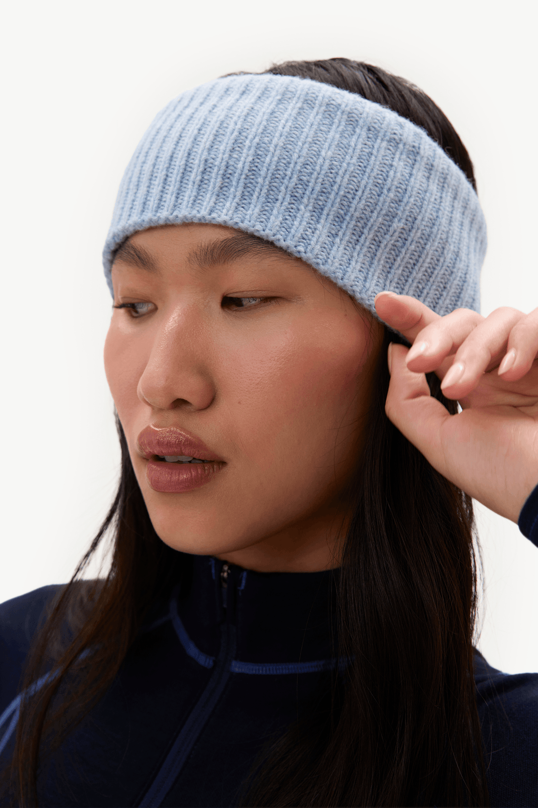 A woman wearing a light blue ribbed knit headband, shown in a close-up profile view against a plain white background.