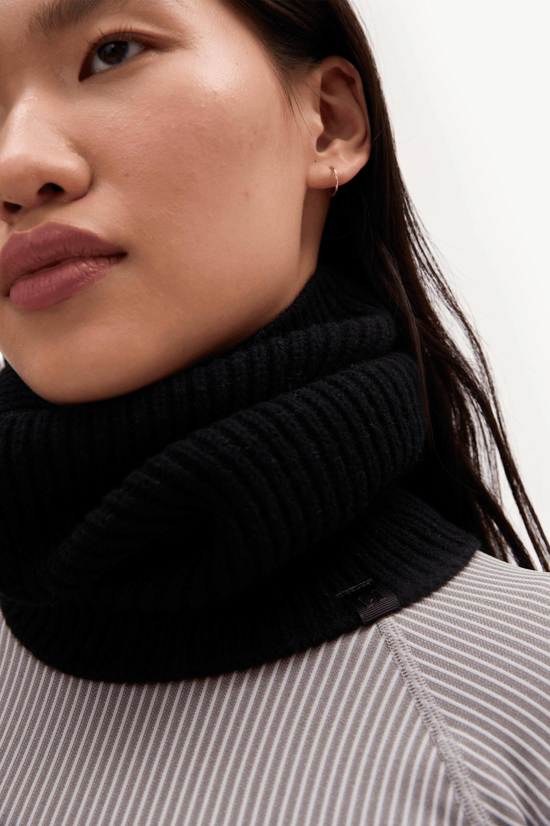Close-up of a model wearing a thick, ribbed black turtleneck scarf or neck warmer over a gray and white striped top.