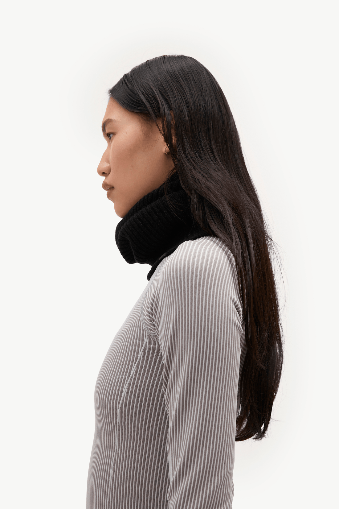 A woman in profile wearing a black ribbed turtleneck sweater against a plain white background.
