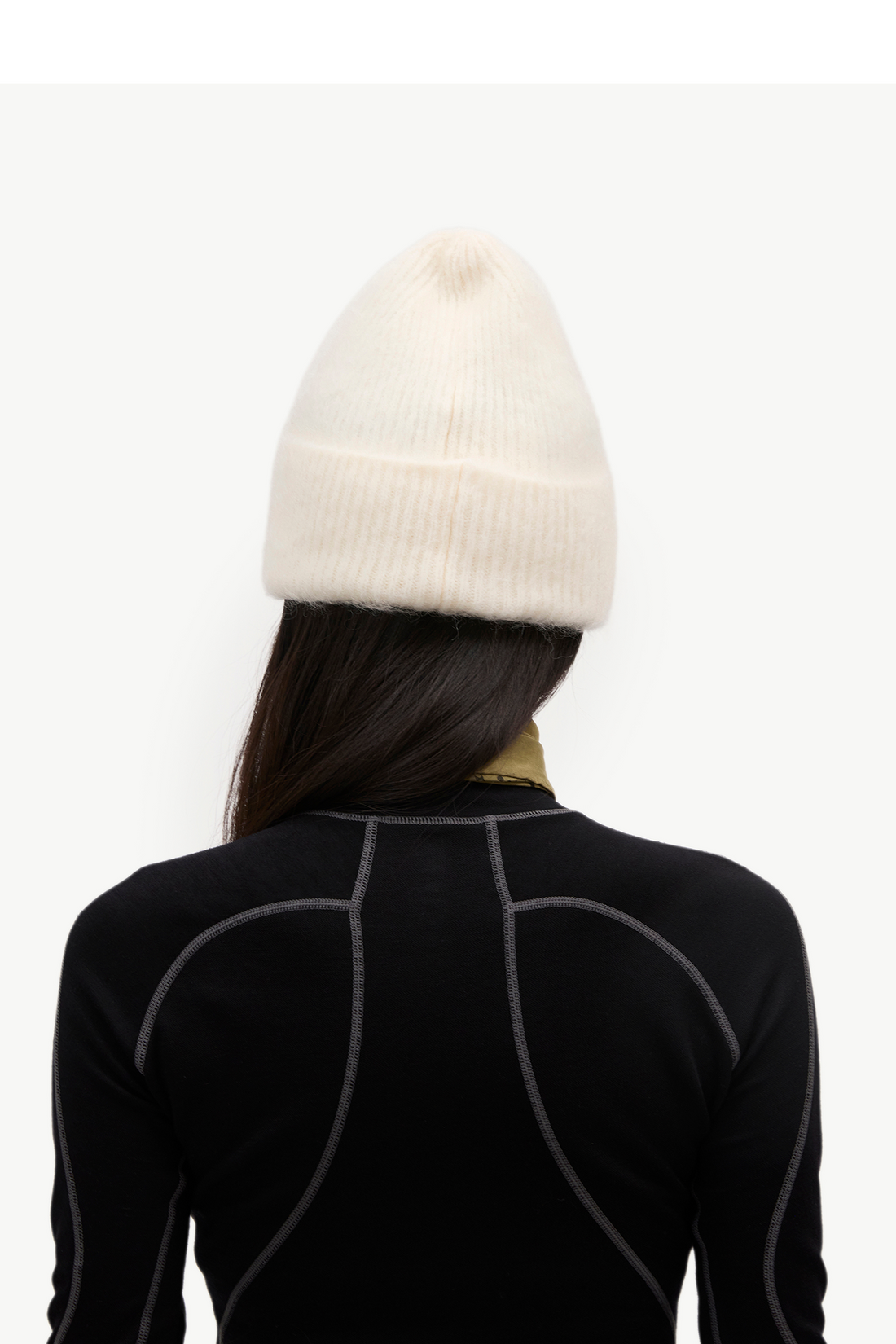 A person shown from the back wearing a cream-colored ribbed knit beanie and a black long-sleeve athletic top with gray seam detailing, against a plain white background.