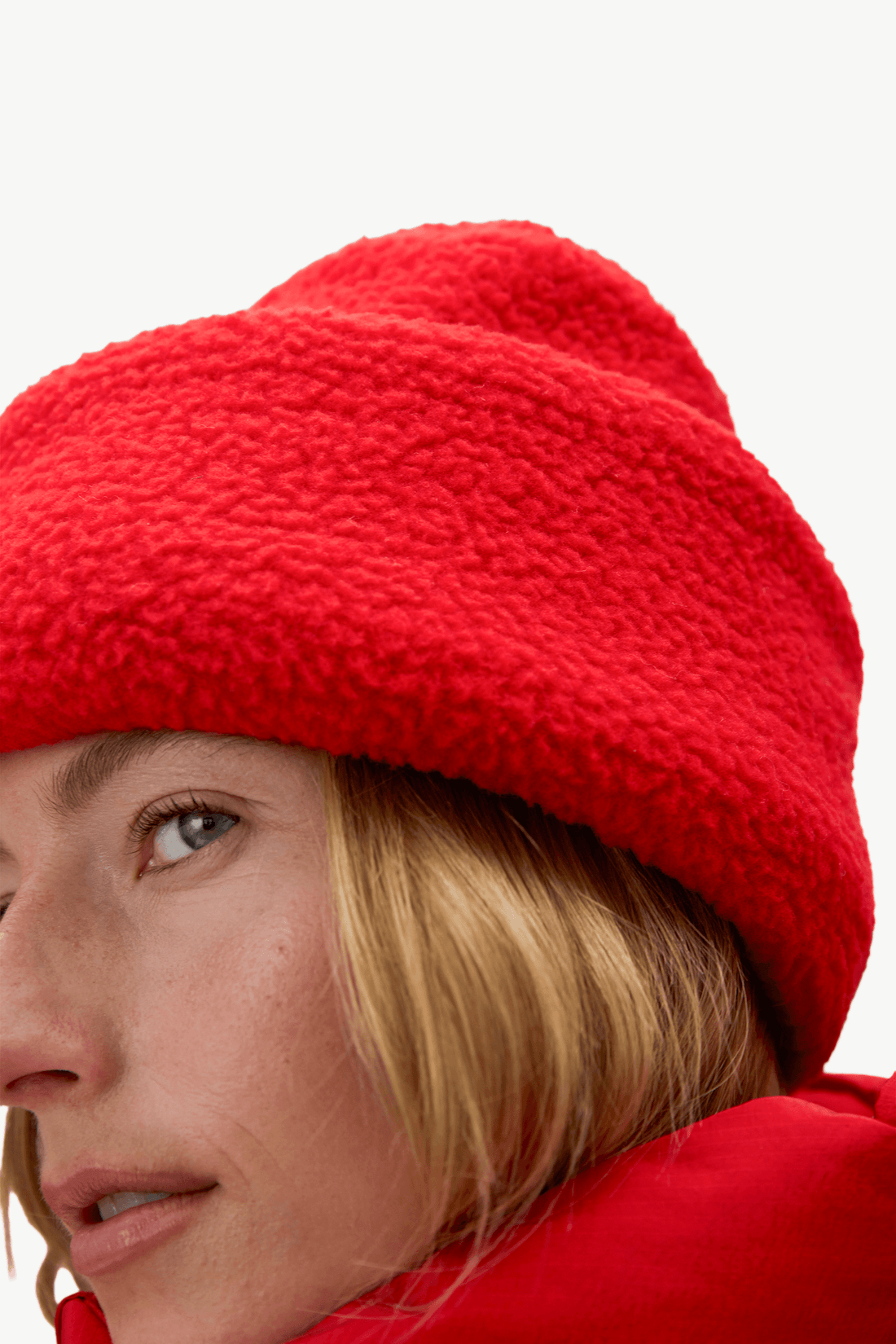 Close-up of a person wearing a bright red textured fleece beanie and a matching red outerwear piece against a plain light background.
