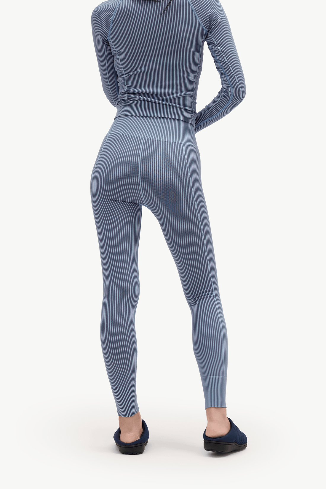 A person shown from the back wearing a matching ribbed long-sleeve top and high-waisted leggings set in a muted blue-gray color, paired with dark slip-on shoes, against a plain light background.