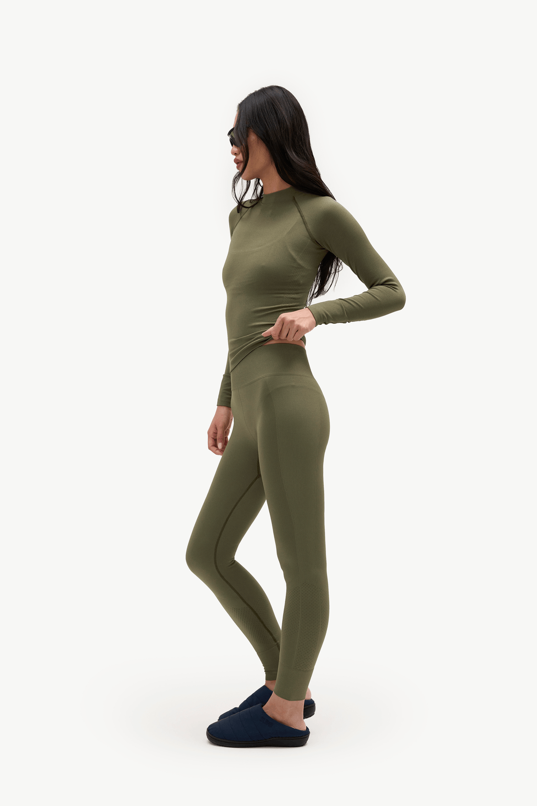 A woman modeling a matching olive green long-sleeve top and leggings set, shown in profile against a plain white studio background.