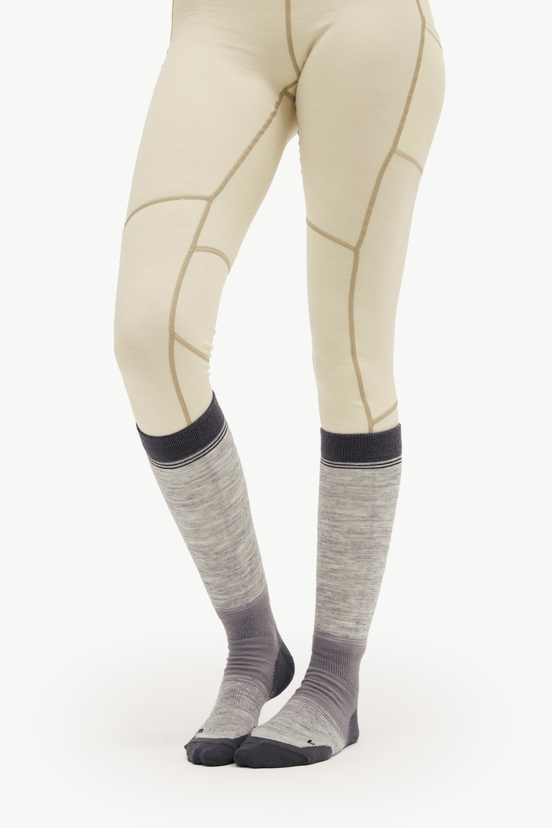A person wearing light beige fitted leggings with tan seam lines and gray knee-high socks with dark gray toes and cuffs, shown against a plain white studio background.