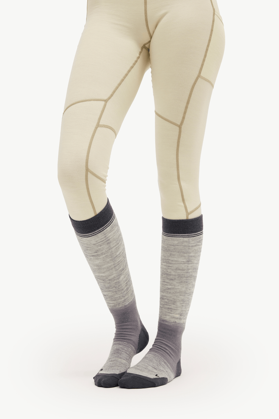 A person wearing light beige fitted leggings with tan seam lines and gray knee-high socks with dark gray toes and cuffs, shown against a plain white studio background.