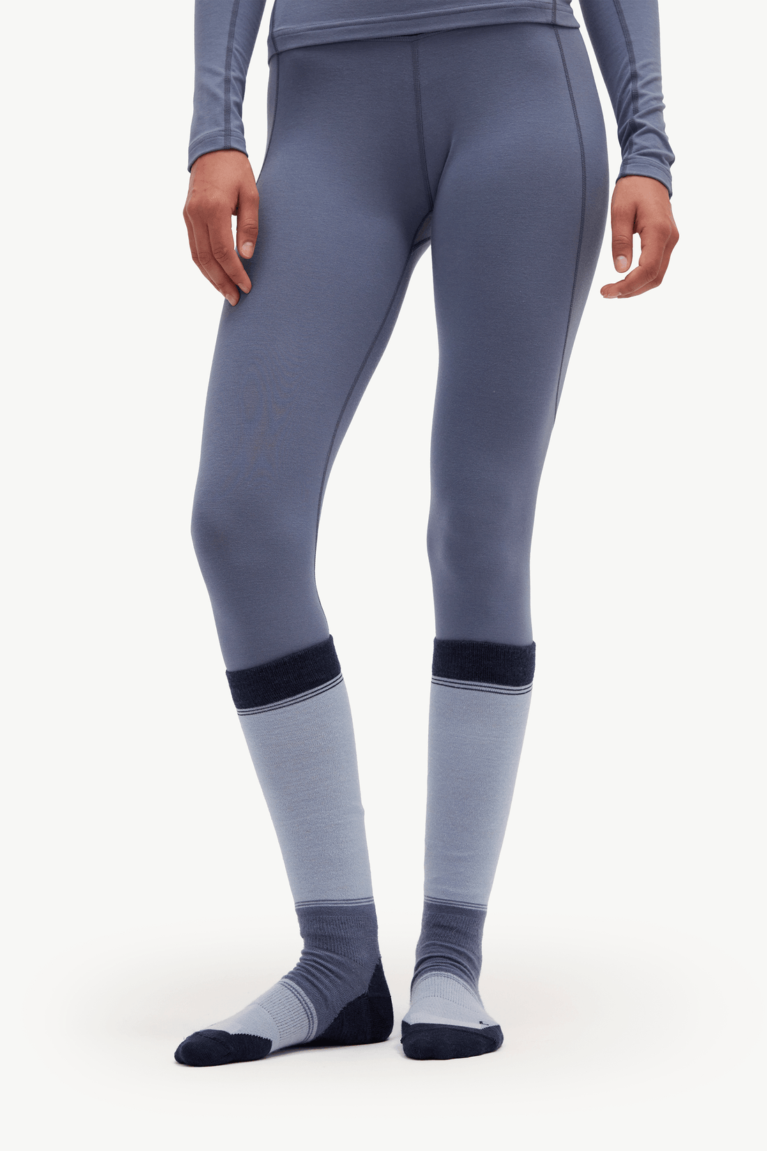 A model wearing slate blue-gray athletic leggings with dark navy ribbed cuffs and matching gray and navy socks, shown from the waist down on a light gray studio background.